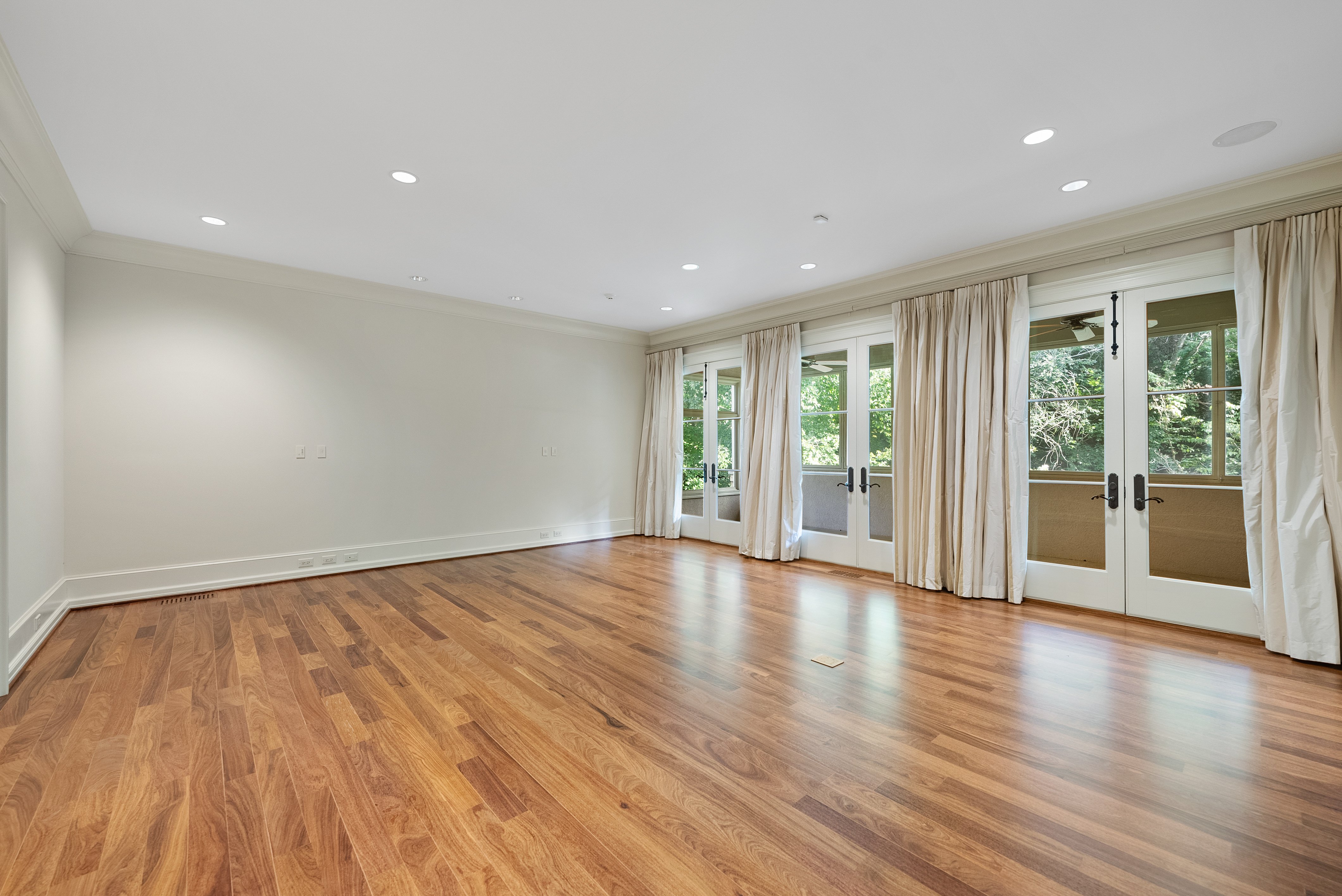 White room with hardwood floors. One wall is all double French doors with curtains.