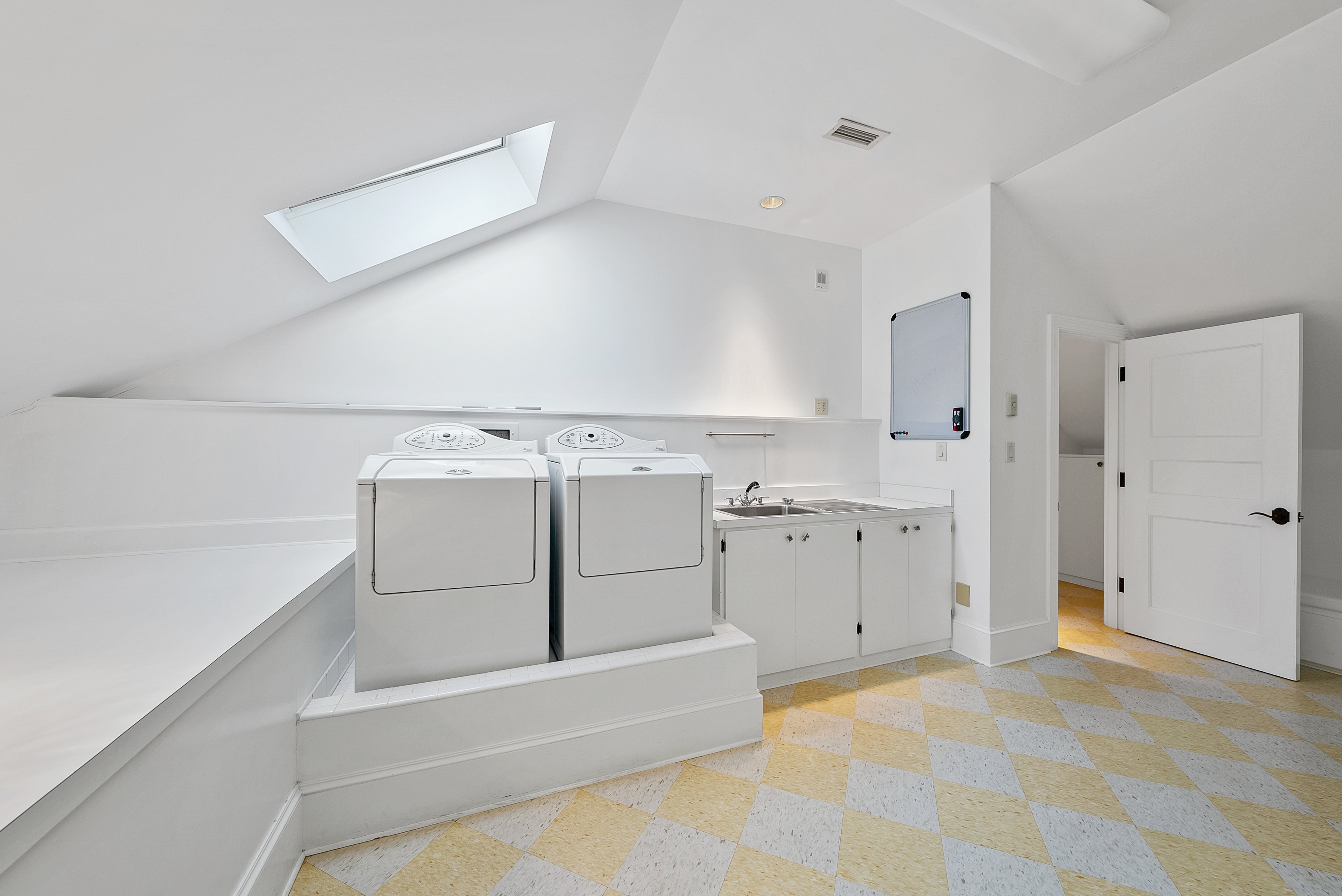 A white laundry room with appliances, a sink, and a skylight in the ceiling.