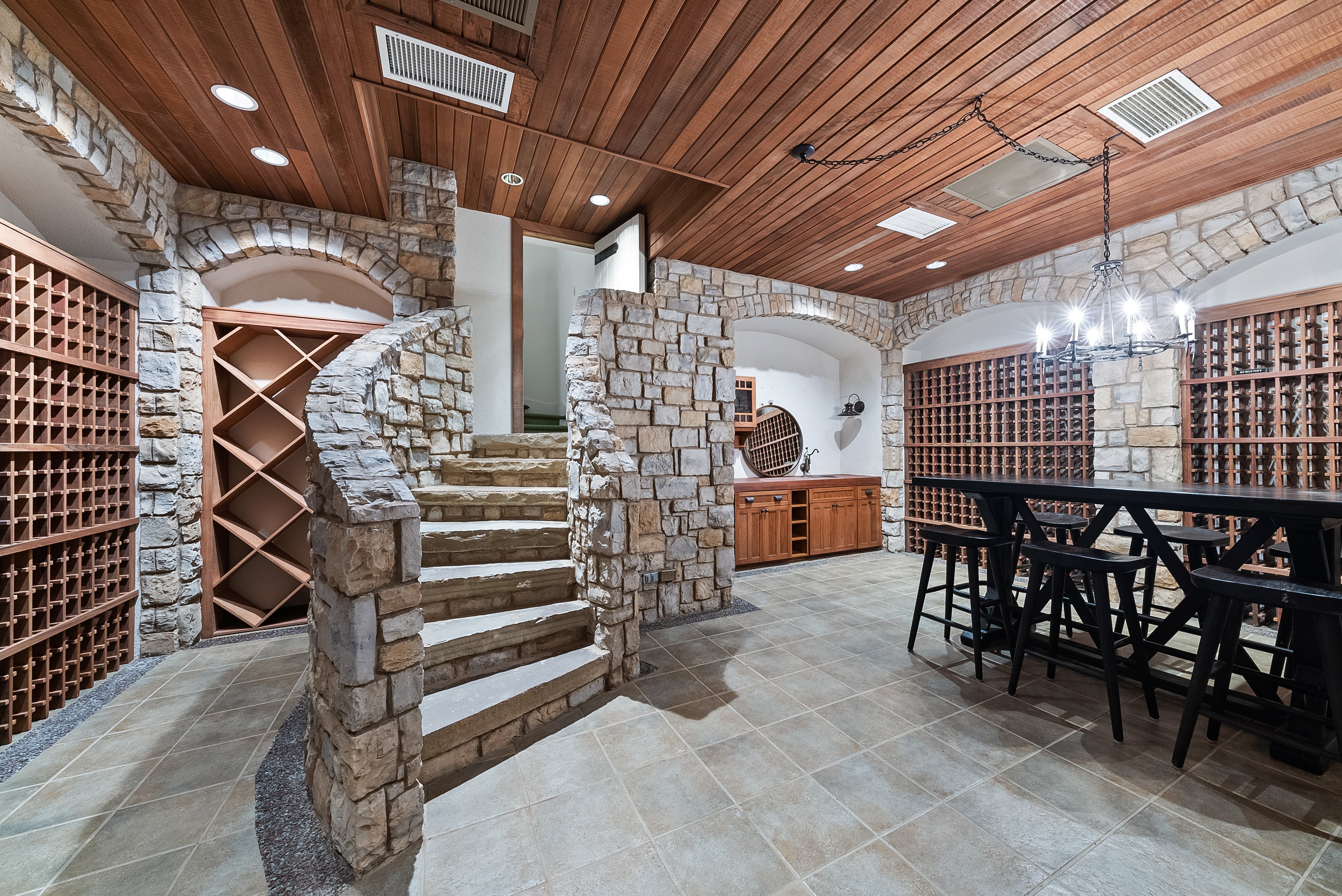 A stone staircase leading into a wine cellar, with a bar-height table and barstools.
