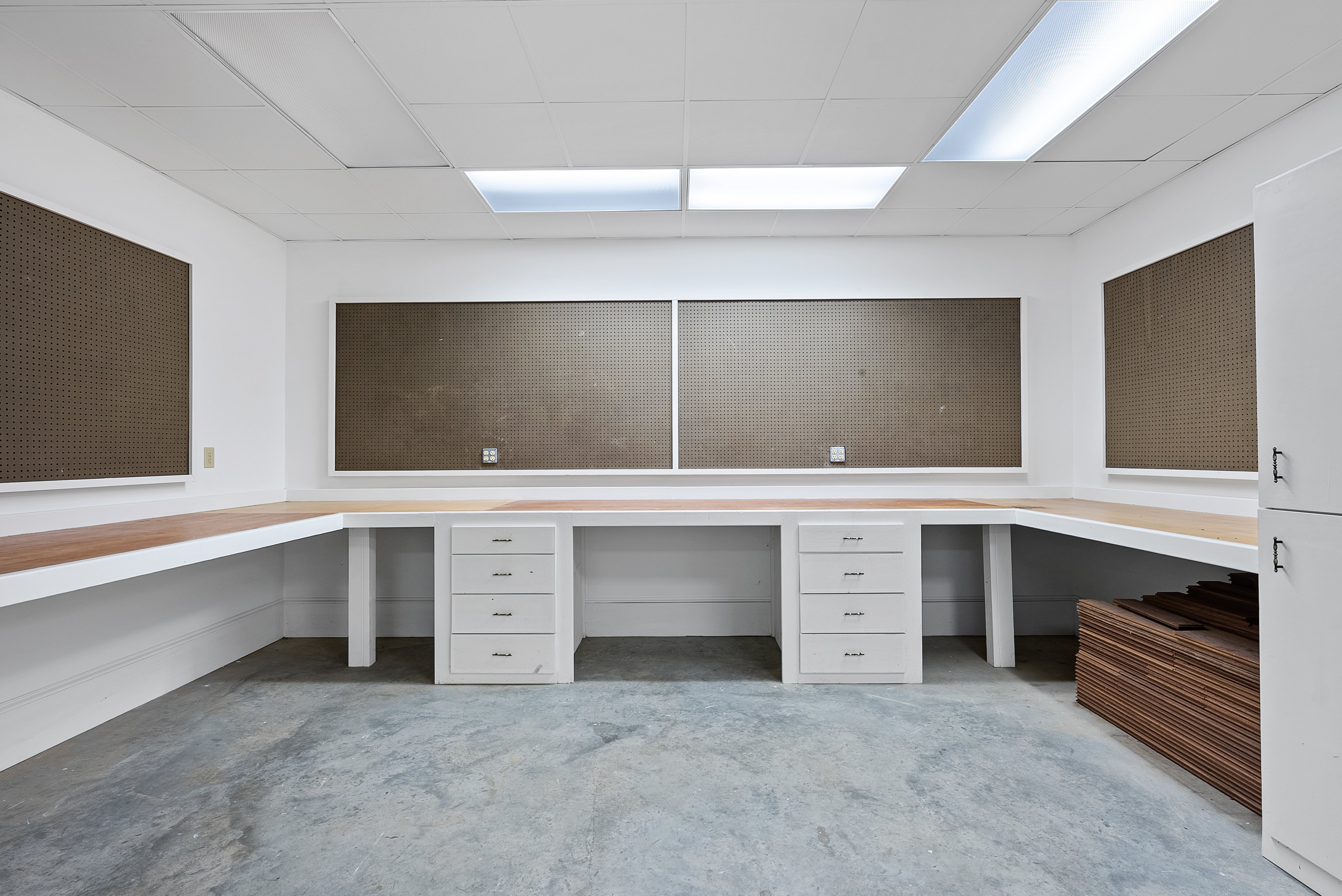 Interior of a study or workshop area. There are work surfaces along each wall, with pegboards above them.