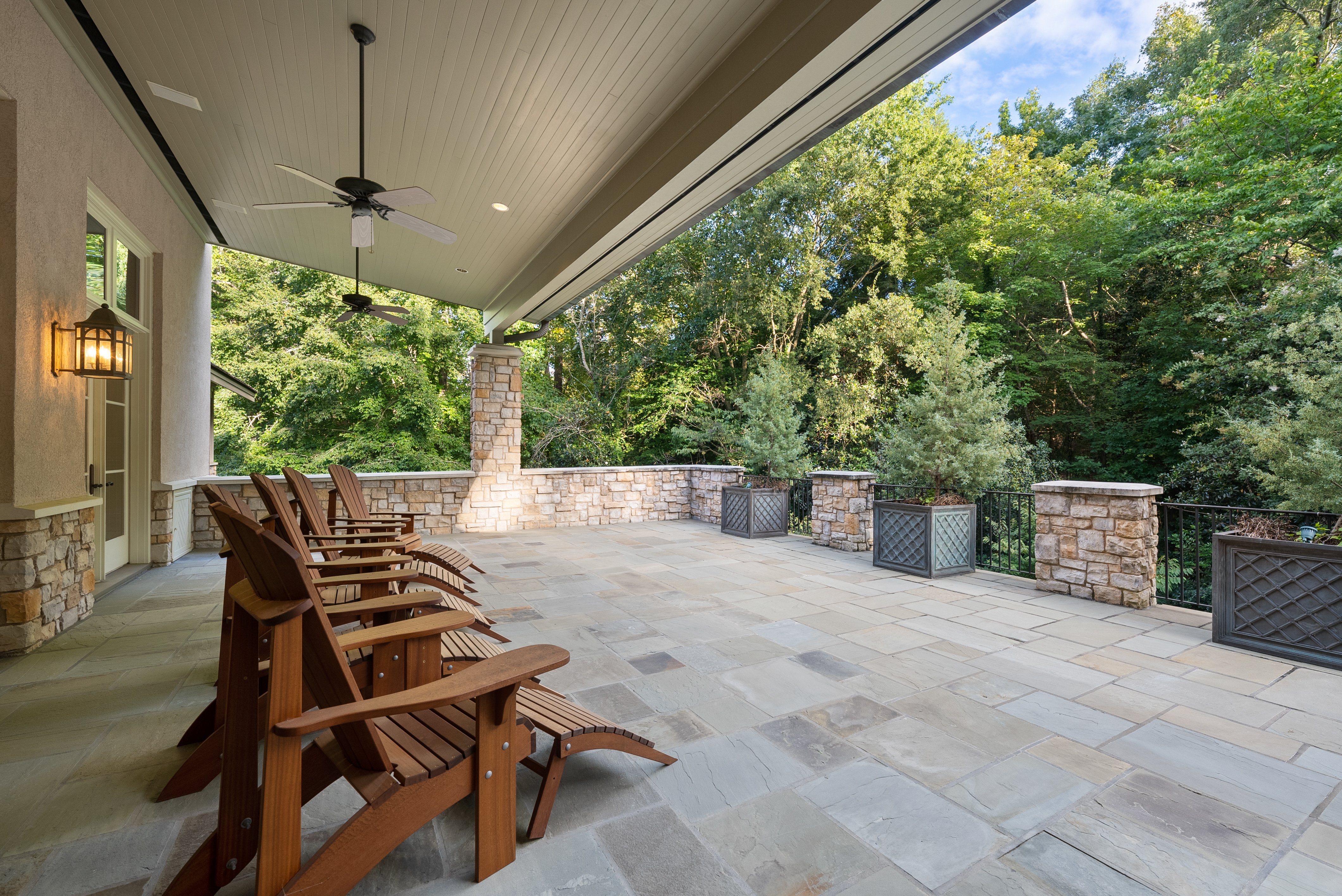 Exterior view of a tiled patio with wooden chairs facing trees