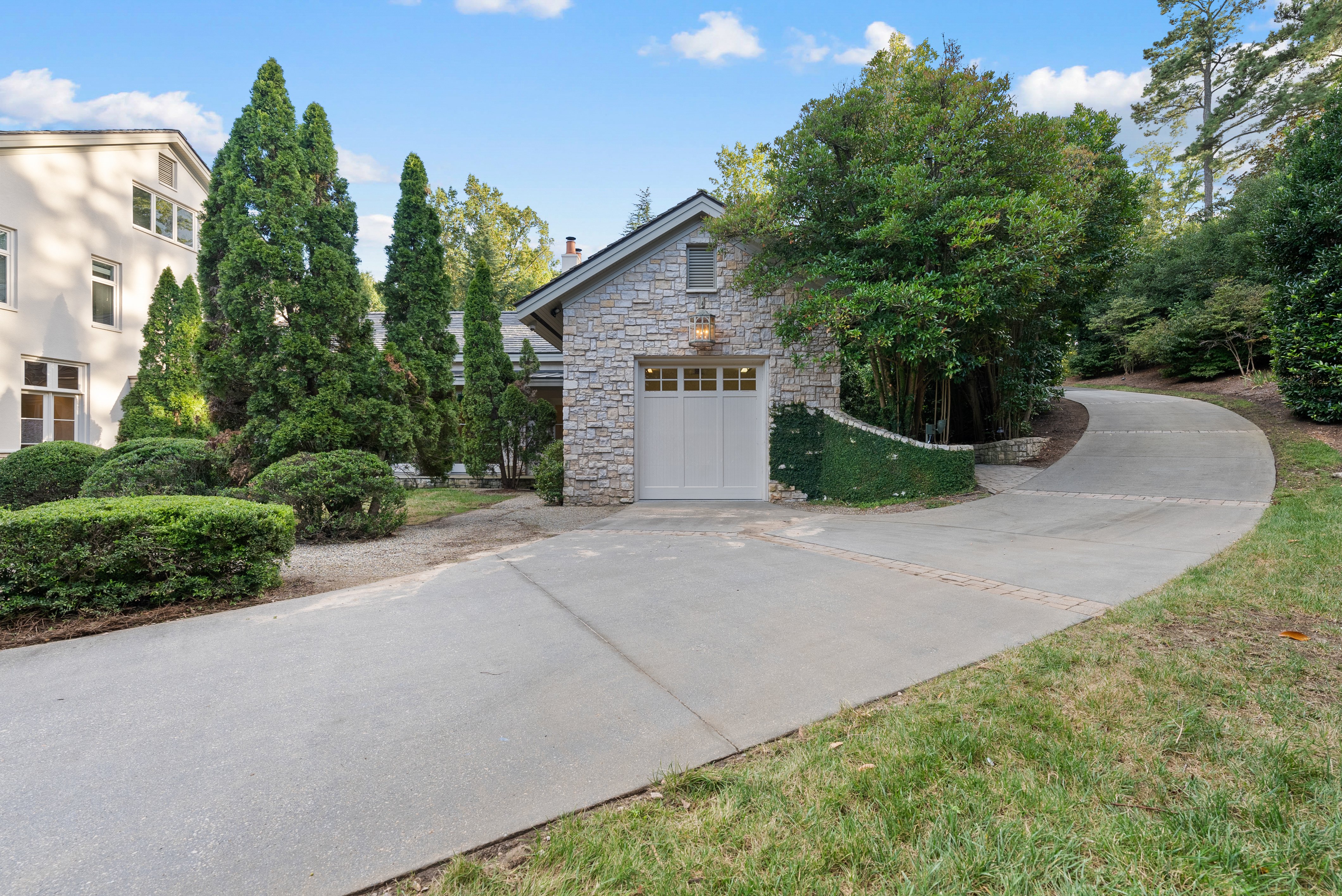 A driveway leading to a small, side garage, with the drive continuing past and up the hill.
