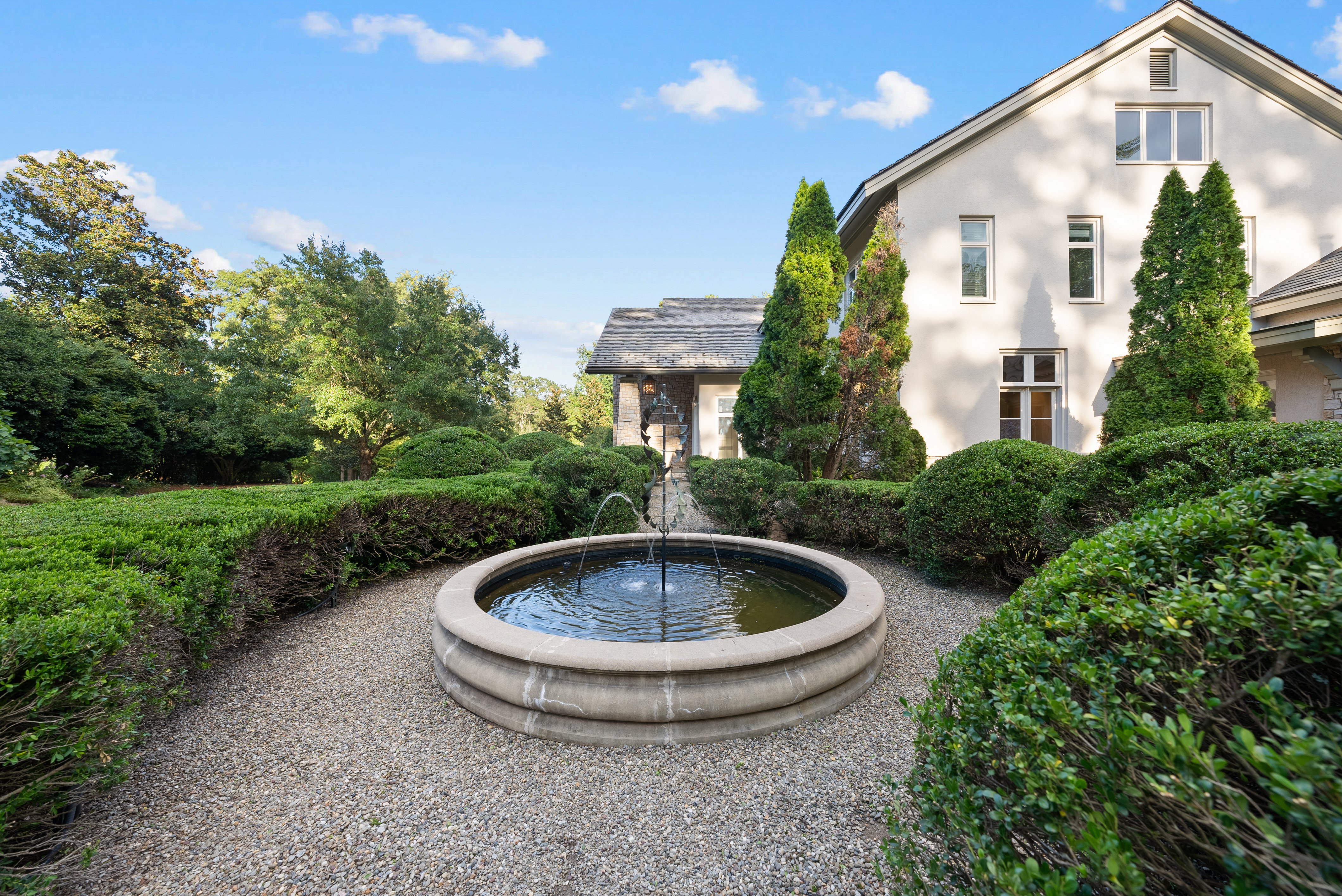 A water fountain with a gravel walkway around it, located in front of the house.