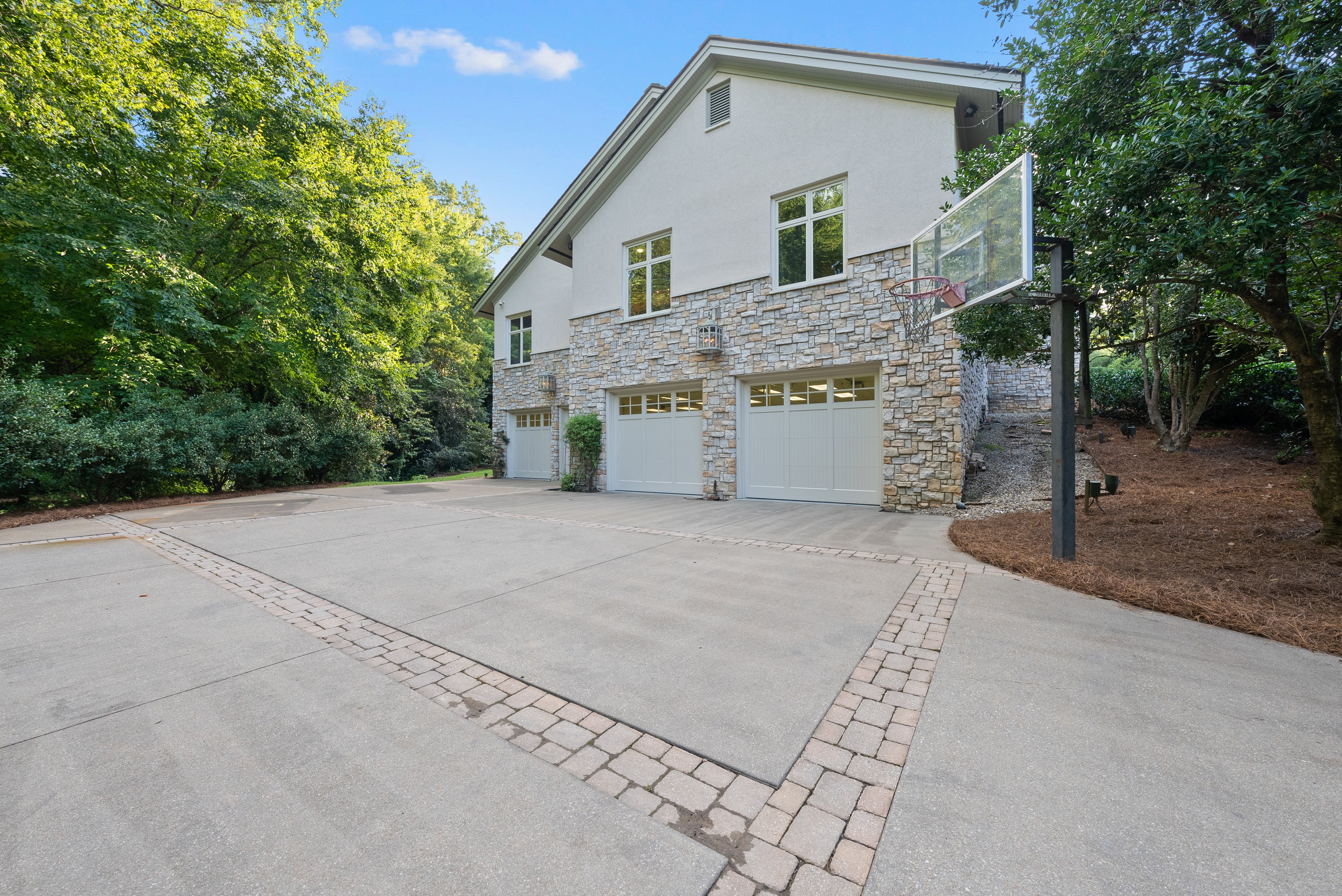 The exterior of the home, showing the four-door garage, a large drive area, and a basketball hoop