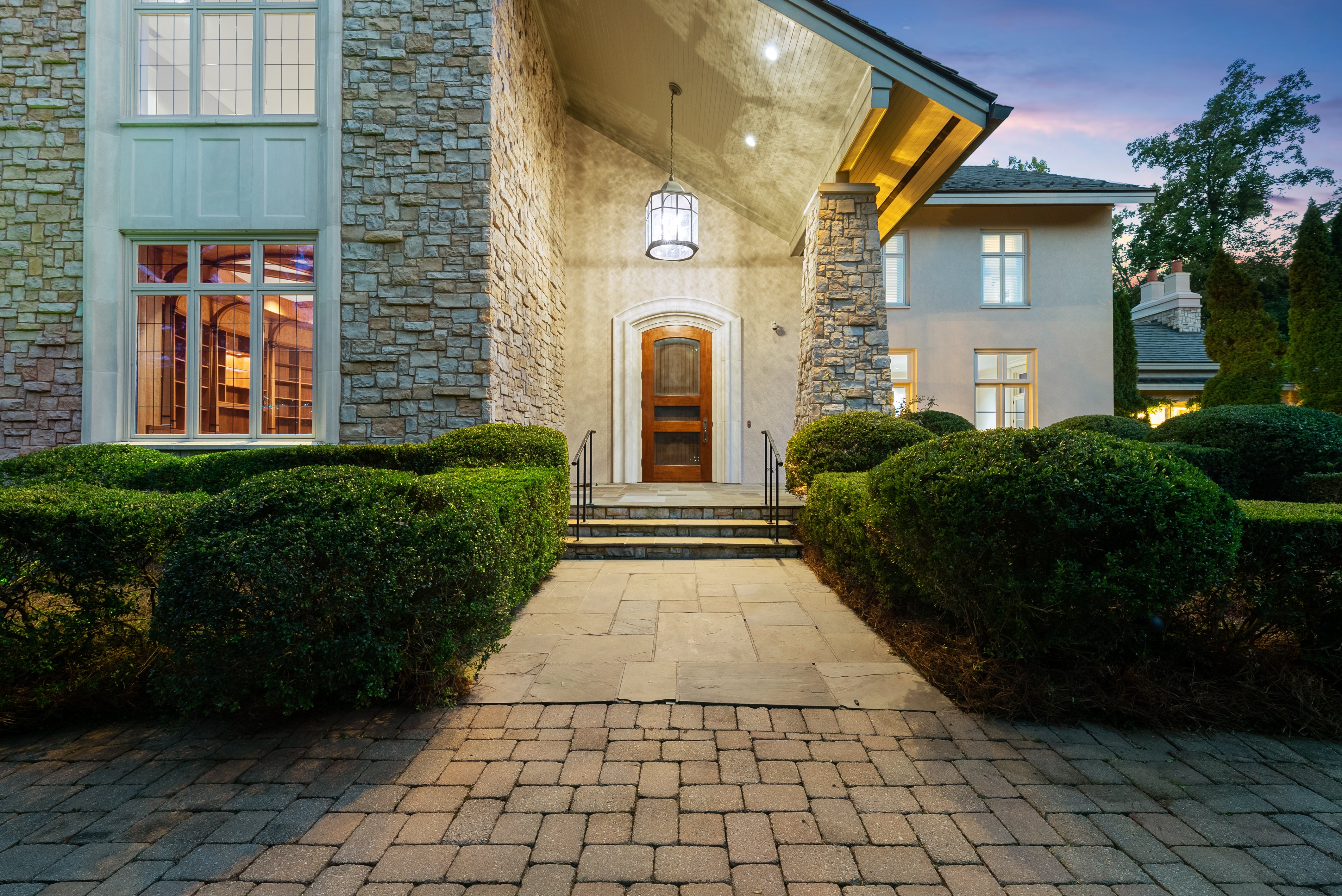 A dusk or twilight view of the front door to the home, shot from the exterior, with an overhead light on.